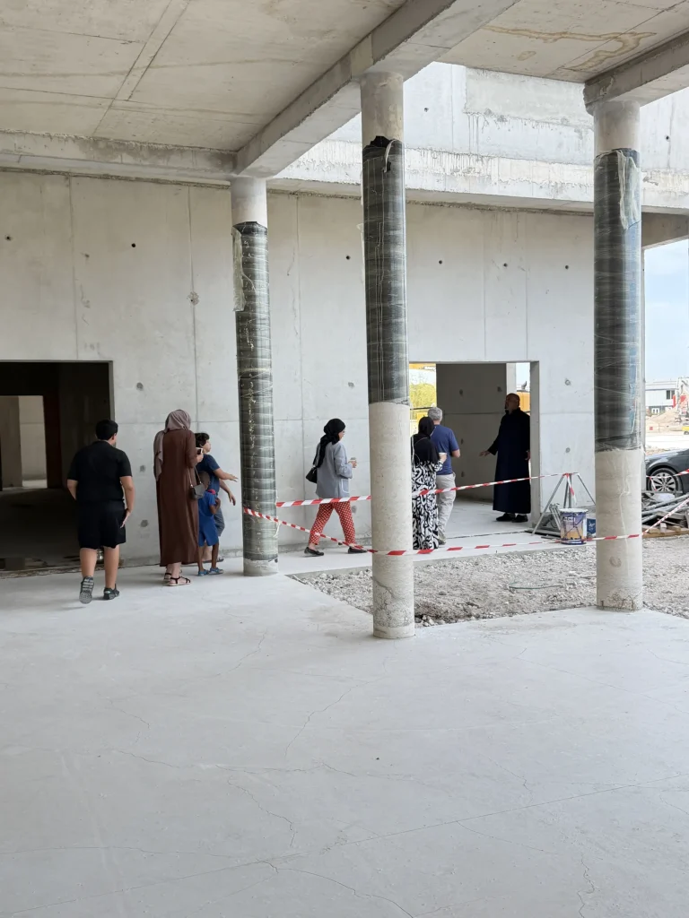 Un groupe de visiteurs, adultes et enfants, avance sous le passage couvert vers une porte du bâtiment.