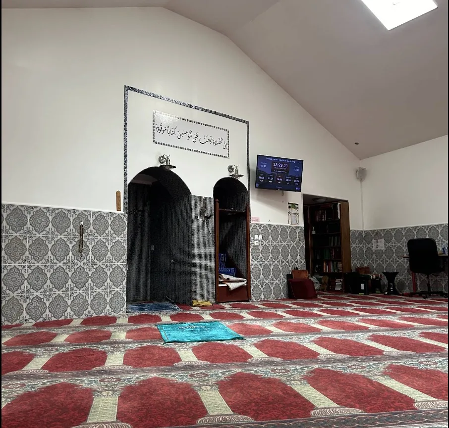 Salle de prière : mihrab carrelé, calligraphie au mur, tapis rouges